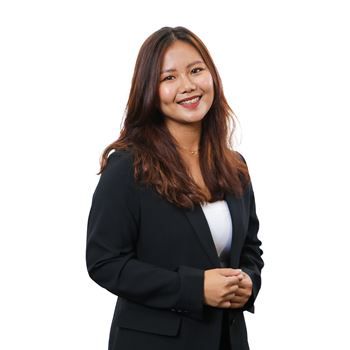 A smiling person with long brown hair, wearing a black blazer over a white shirt, stands against a white background.