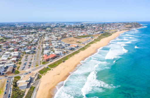 Aerial view of a coastal town beside a sandy beach and turquoise ocean with waves.