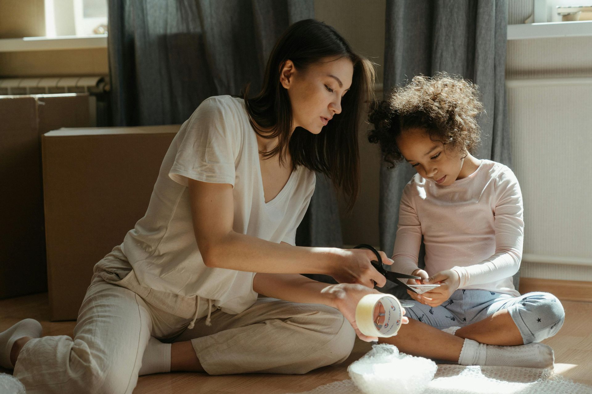 Two people sit on the floor making a craft together with white cotton and paper cups.