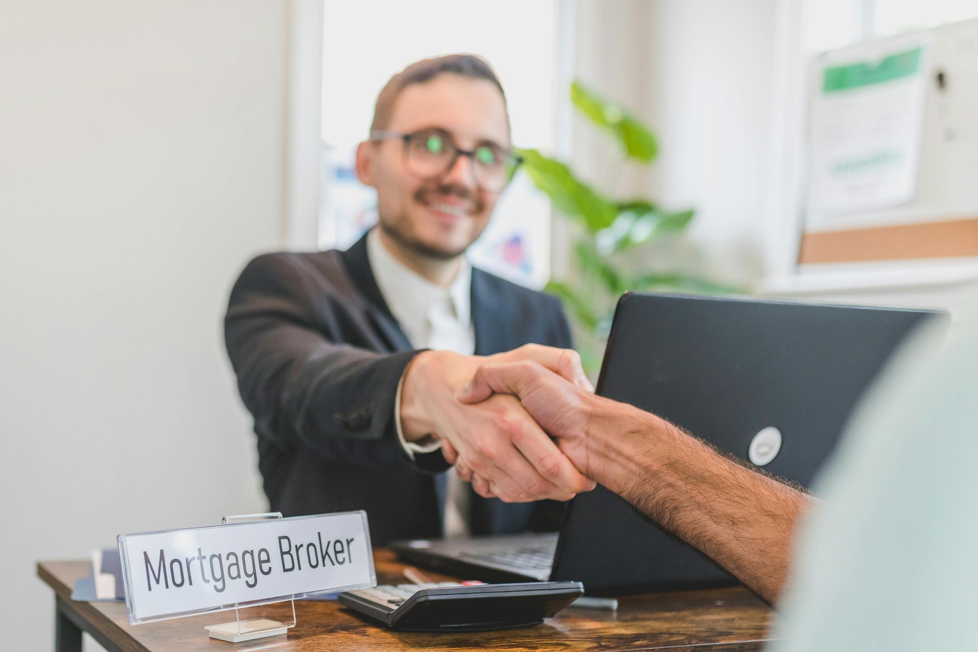 Mortgage broker shaking hands with a client across a desk in an office