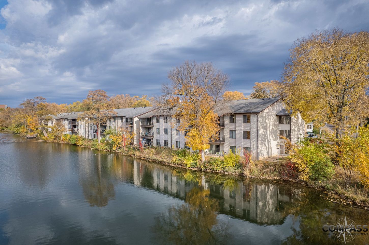 Autumn lakeside apartments with colorful trees and cloudy sky reflected in calm water