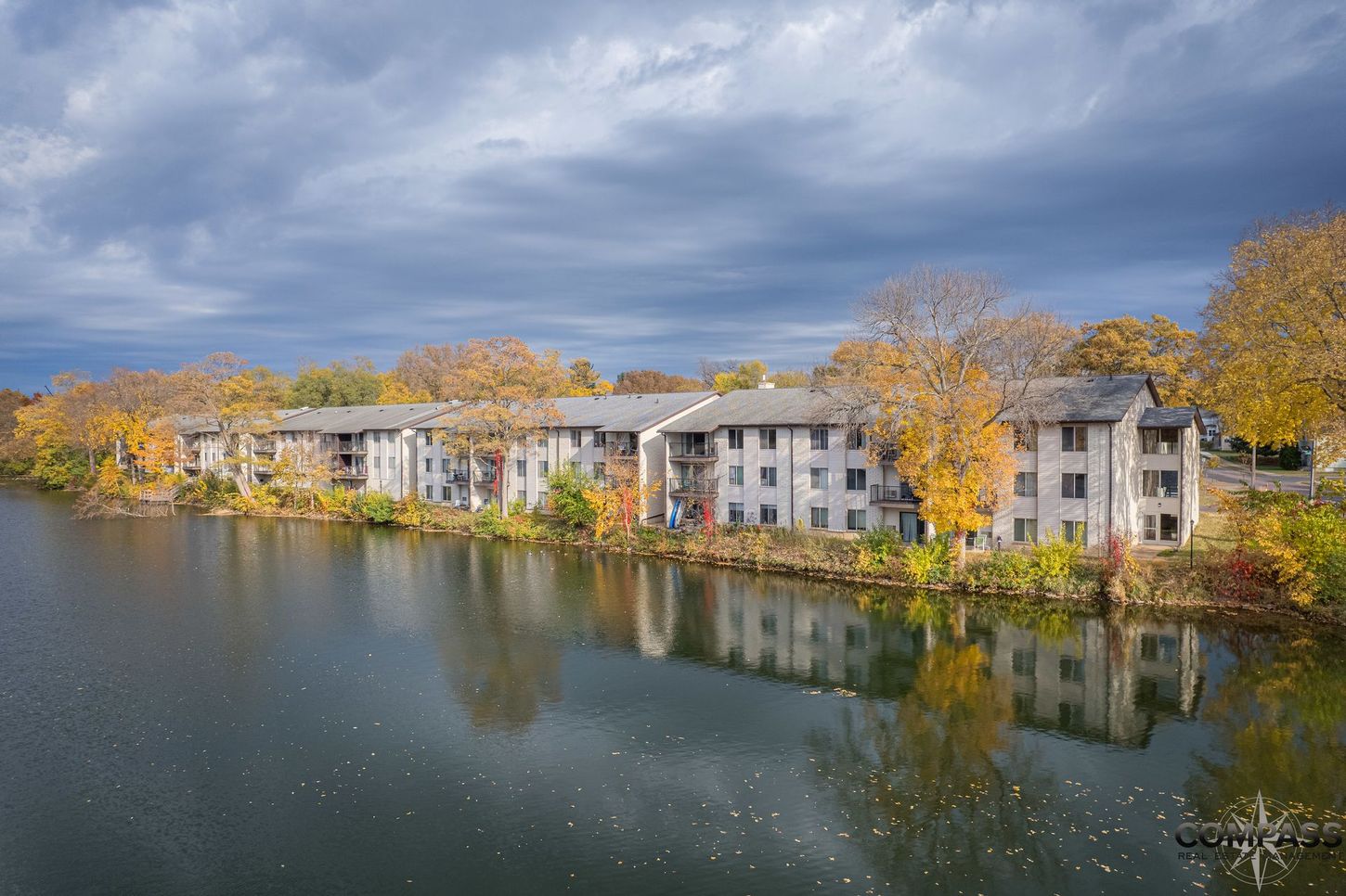 Apartment buildings by a lake with autumn trees and cloudy sky, reflected in calm water