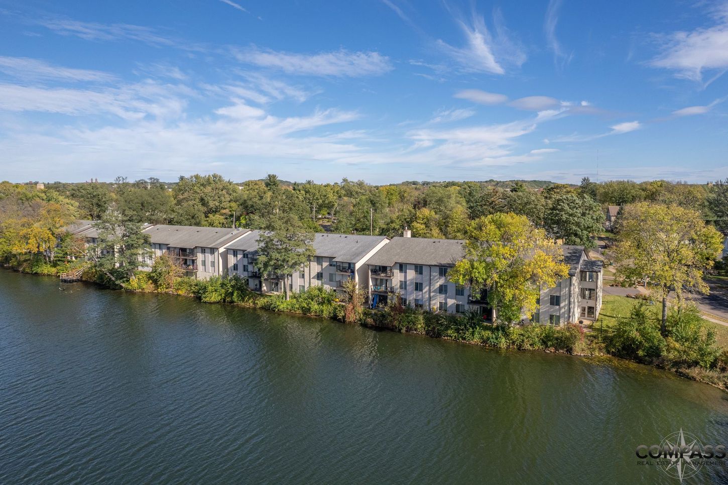 Lakeside apartment buildings with balconies beside a calm body of water under a blue sky