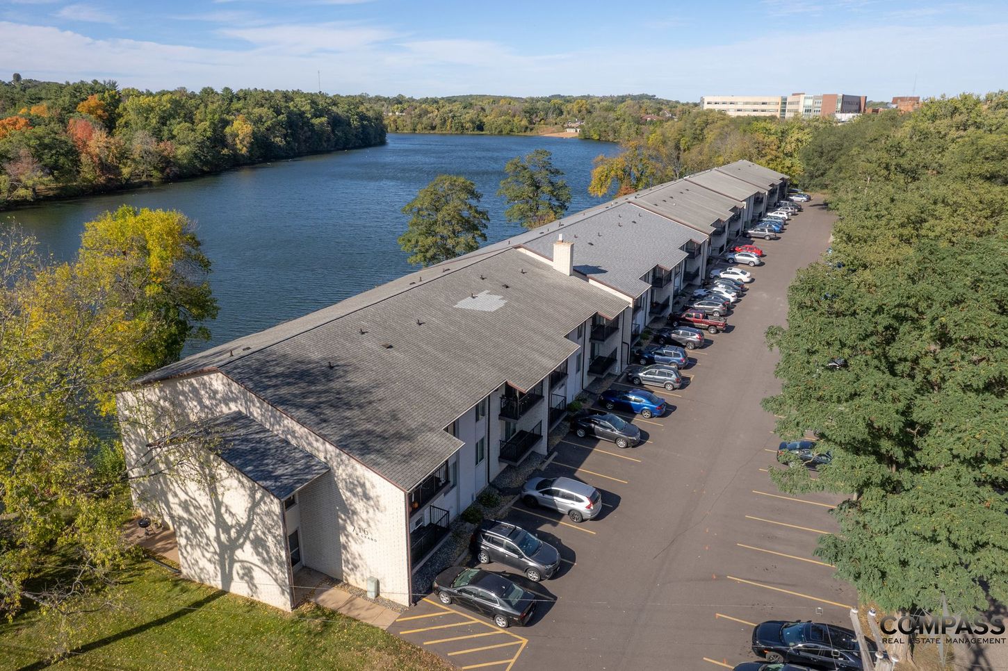 Aerial view of a long office building beside a river, with a parking lot and trees in autumn.