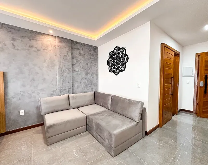 Um sofá de canto moderno em uma sala cinza-clara com uma parede de destaque texturizada em cinza e uma decoração de parede com mandala preta.