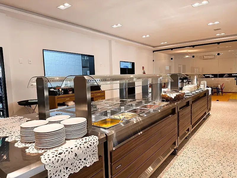 Um balcão de buffet com pilhas de pratos brancos sobre uma toalha de mesa de renda em uma área de jantar limpa, moderna e bem iluminada.