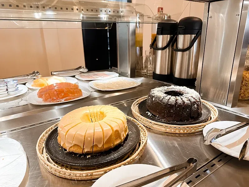 A mesa de bufê apresenta um bolo Bundt de baunilha com cobertura, um bolo Bundt de chocolate e pratos com frutas fatiadas variadas.