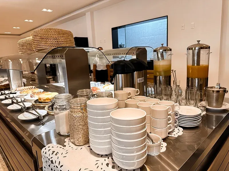 Um buffet de café da manhã com pilhas de tigelas brancas, dispensadores de suco, garrafas térmicas de café e potes de grãos.