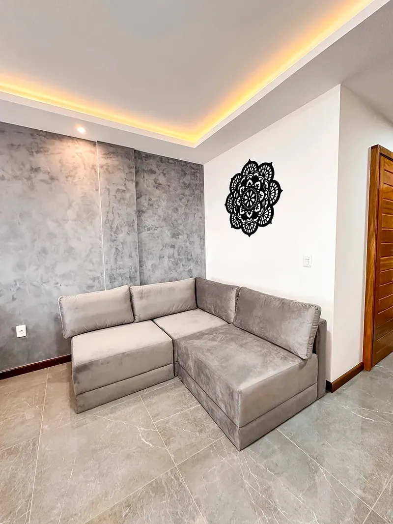 Um sofá modular moderno cinza ocupa um canto junto a uma parede com textura de concreto, iluminação ambiente no teto e obras de arte na parede.
