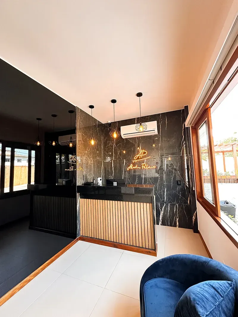 Uma elegante mesa de recepção com frente texturizada em dourado e parede de mármore preto em uma sala moderna com uma poltrona de veludo azul.