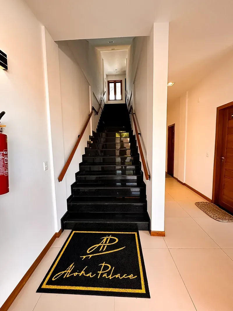 Escadaria de mármore preto com corrimão de madeira e um tapete com a marca 