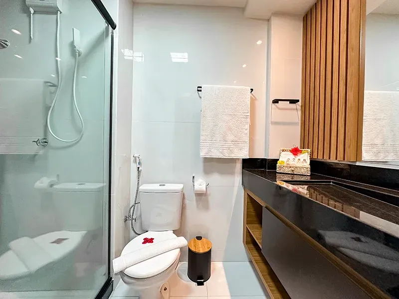 Um banheiro limpo e moderno com box de vidro, vaso sanitário branco e bancada com detalhes em ripas de madeira.