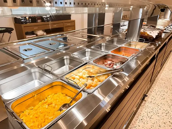 Estação de aquecimento de alimentos em aço inoxidável para buffet, com vários recipientes contendo diversos alimentos preparados.