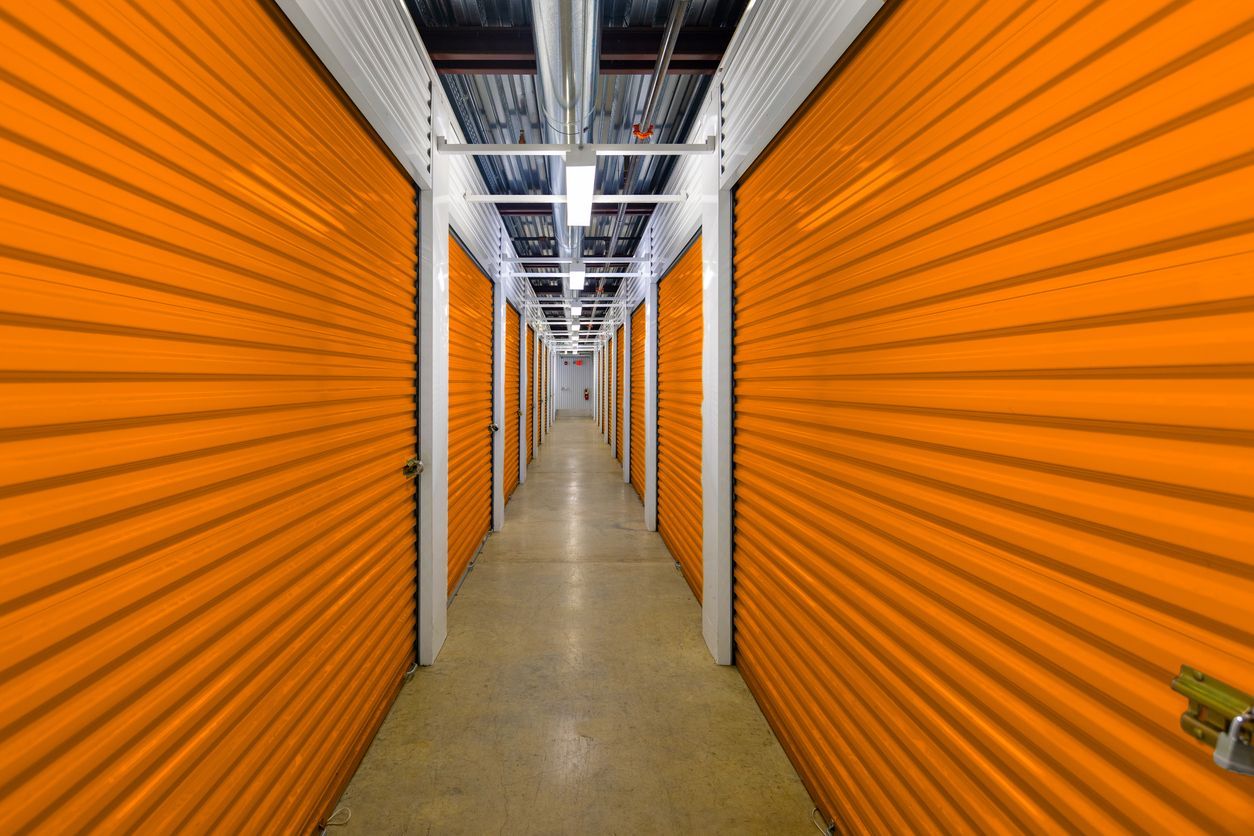  Interior hallway of a self storage facility lined with orange roll-up unit doors on both sides that