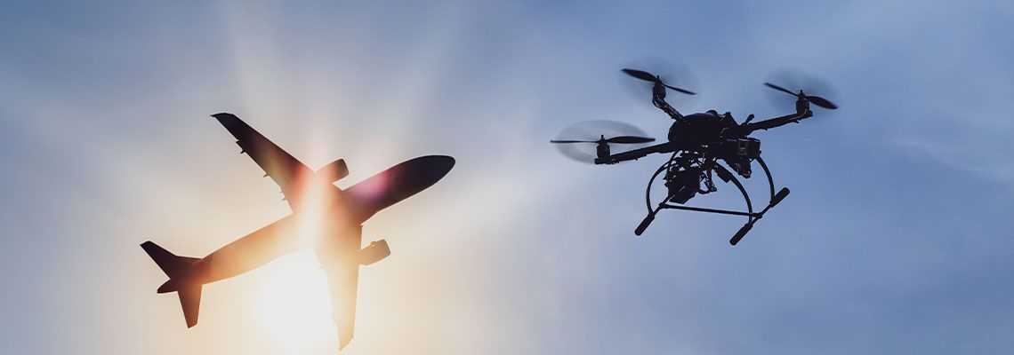 Jet silhouette against the sun beside a drone in a blue sky