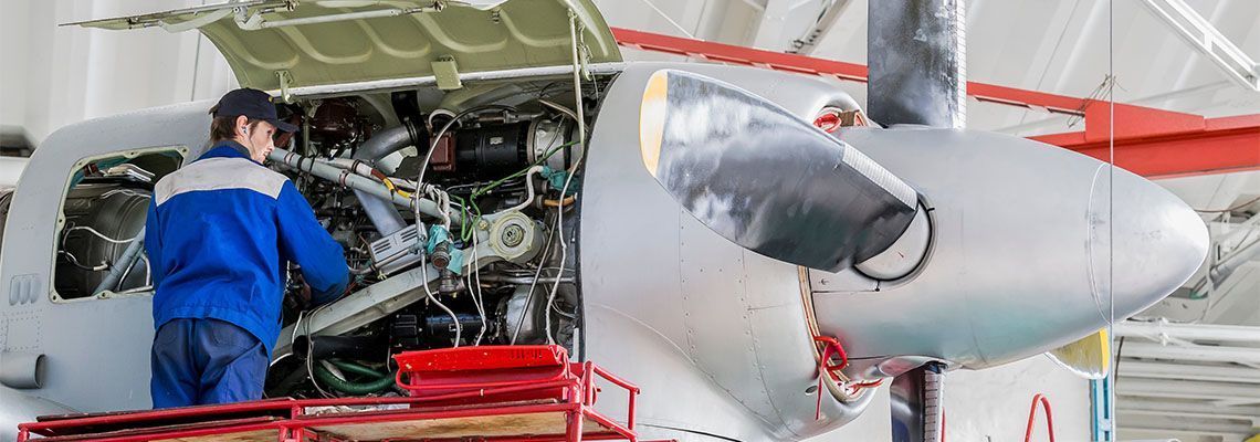 Technician inspecting aircraft engine beside a large propeller in a hangar