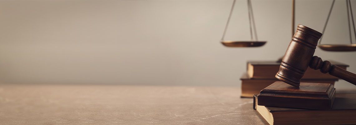 Wooden judge’s gavel resting on law books beside a balance scale on a desk