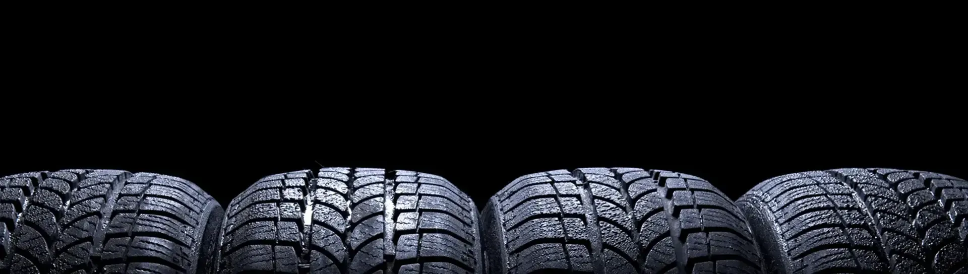 Four car tires lined up against a black background, lit from above