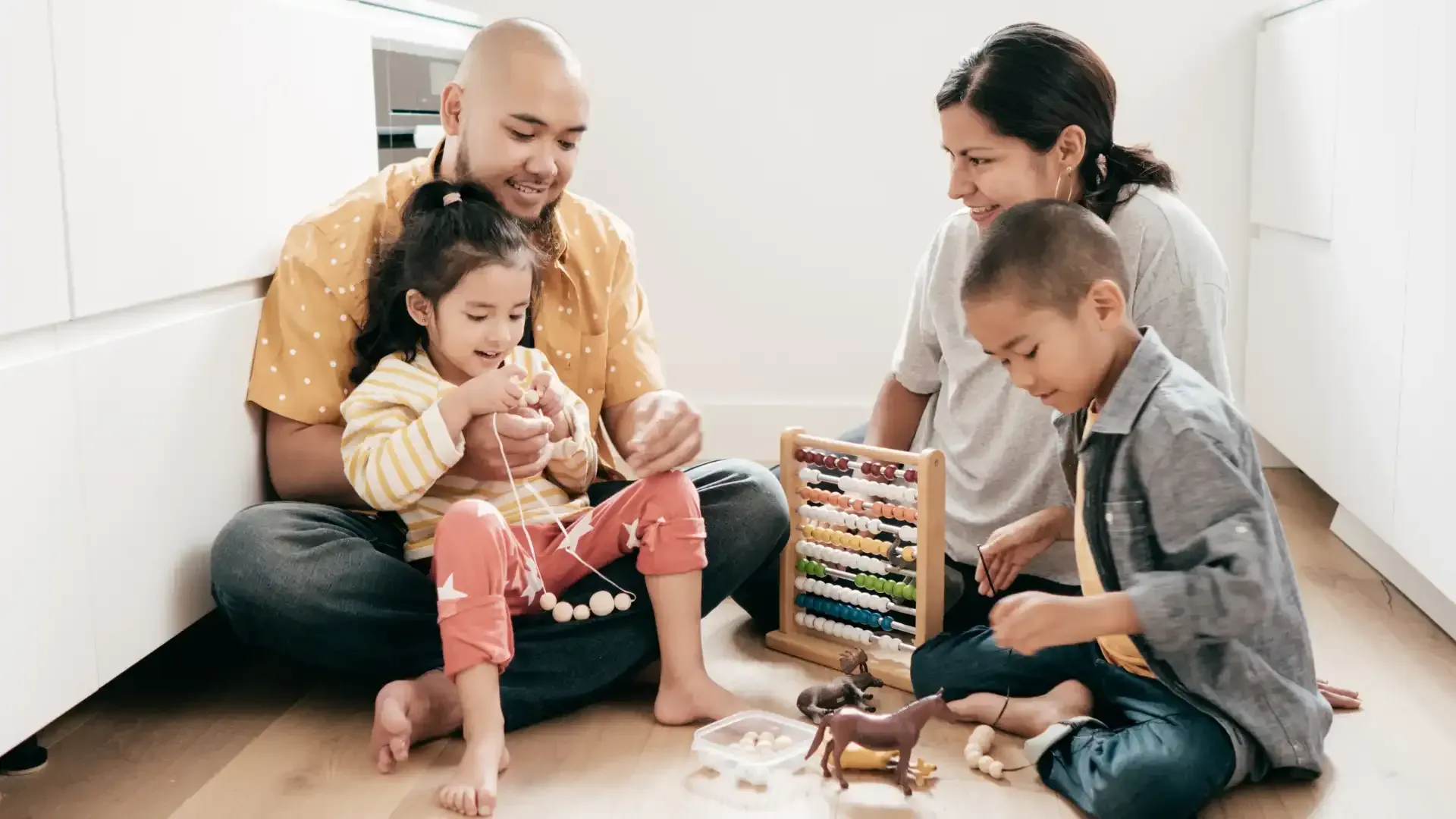 Family sitting on the floor, playing with toys and abacus. Smiling. White interior.