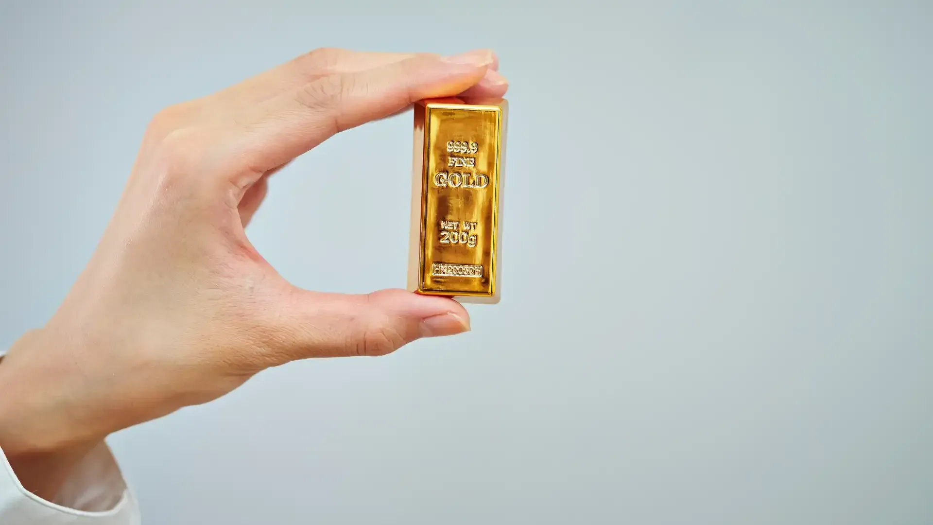 Hand holding a gold bar against a light gray background.