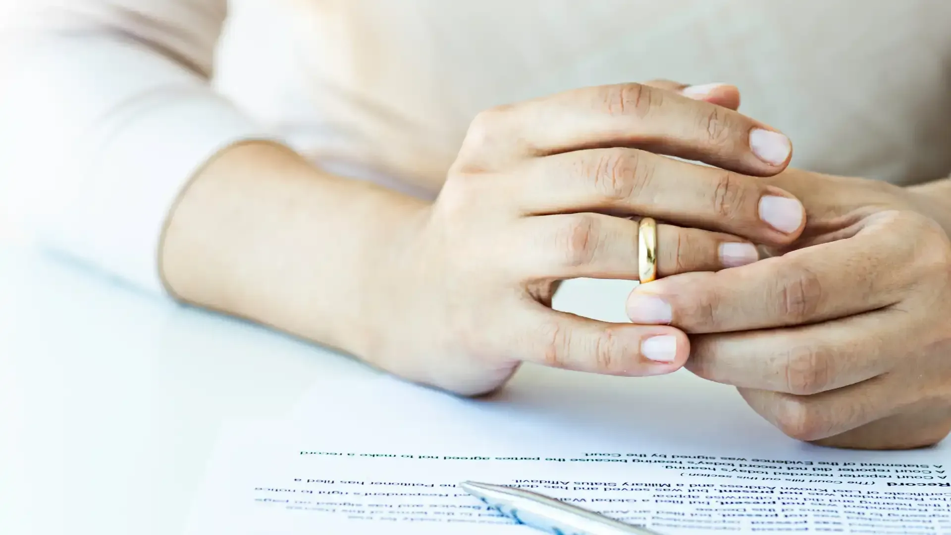 Person removing wedding ring, with divorce papers in view.