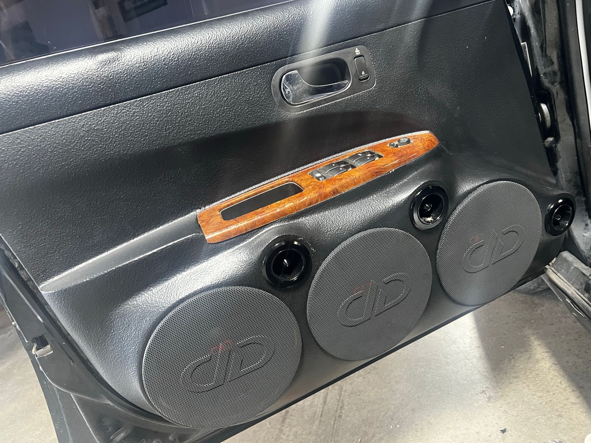 A car door with speakers and a wooden control panel.