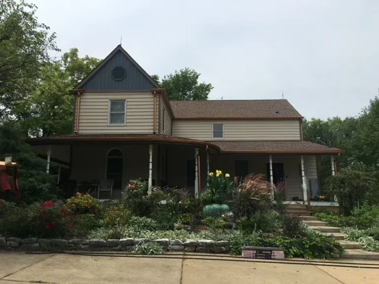 A large house with a porch and stairs is surrounded by trees and bushes.