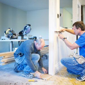 Two men are working on a door in a room.