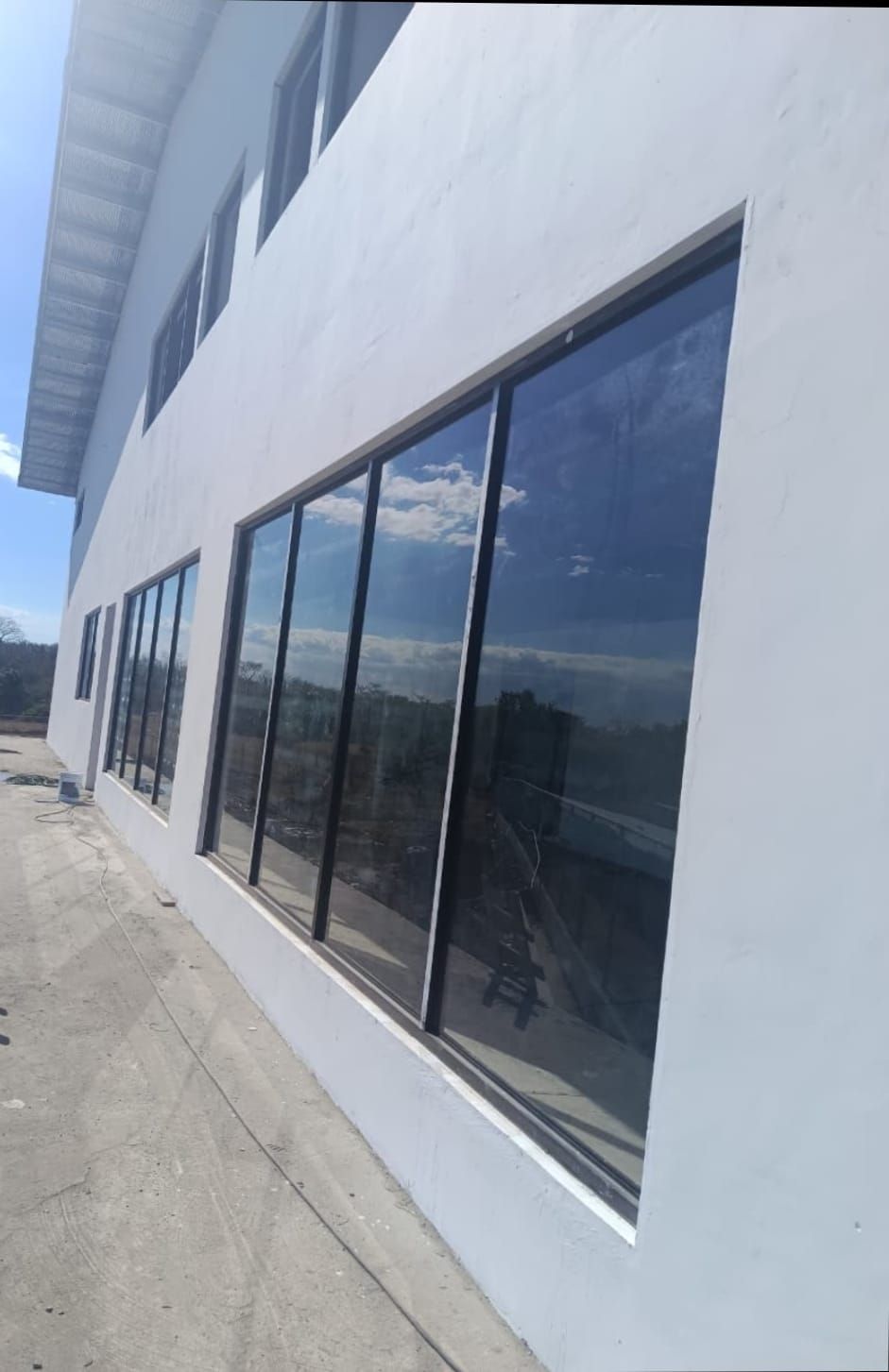 Edificio blanco con grandes ventanas reflectantes a lo largo de una acera bajo un cielo azul.