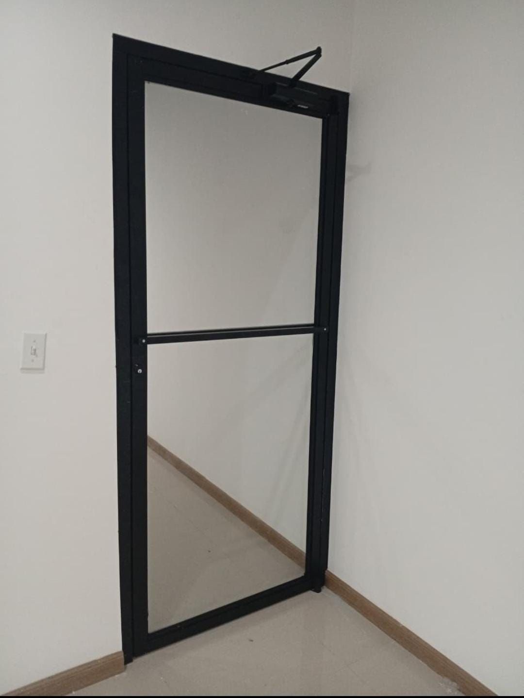 Puerta con marco negro en una habitación blanca lisa, con una abertura estrecha y molduras del suelo visibles.