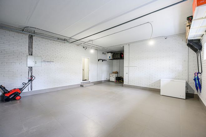 Spacious empty garage with white brick walls, gray floor, and a red lawn mower on the left.