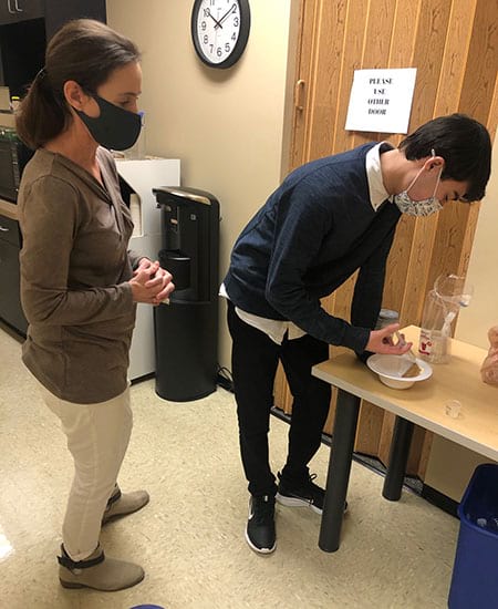 A man and a woman wearing face masks standing next to a table