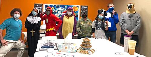 A group of people wearing masks are standing around a table.
