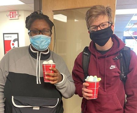 A man and a woman wearing masks are holding cups of ice cream.