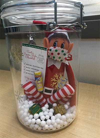 An elf on the shelf wearing a mask is in a jar.