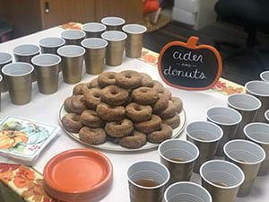 A table topped with a plate of donuts and cups of cider.