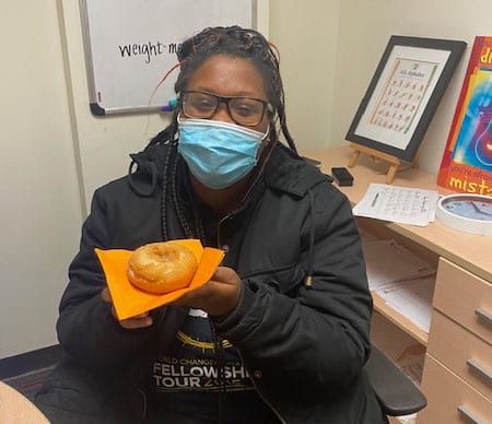 A woman wearing a mask is holding a donut on an orange napkin.