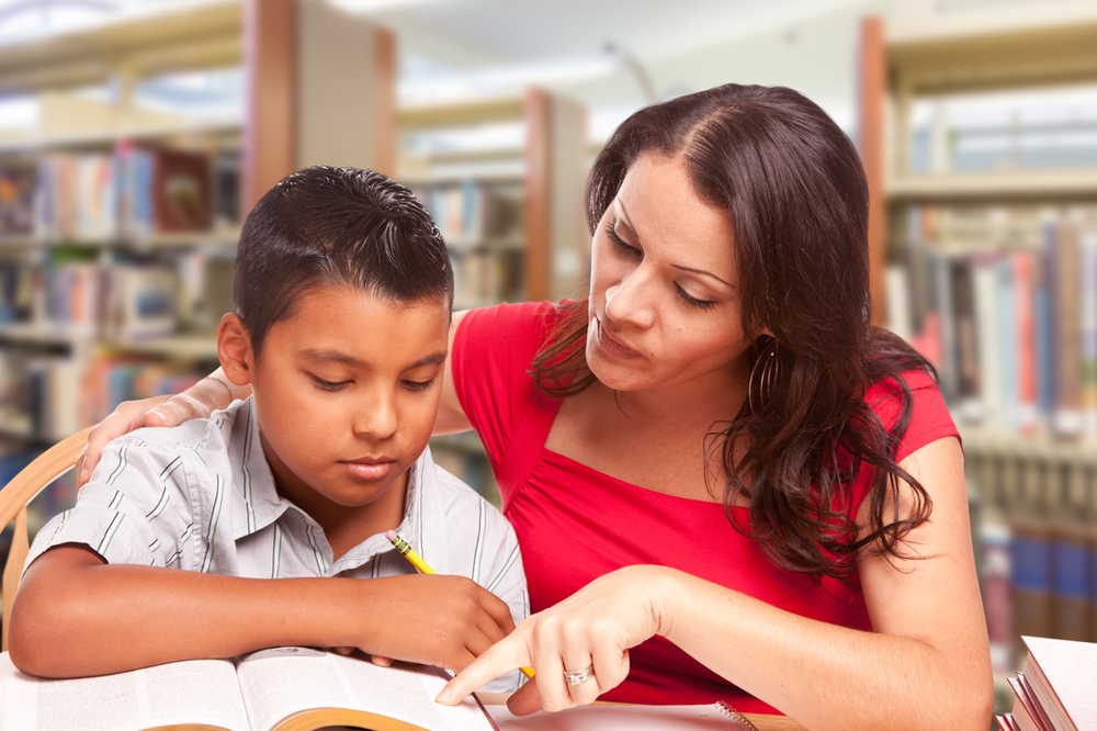 A woman is helping a young boy with his homework in a library.