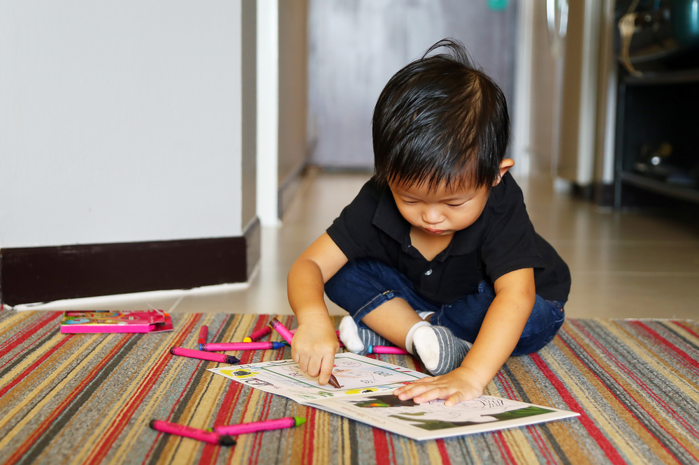 A young boy is sitting on the floor drawing with crayons.