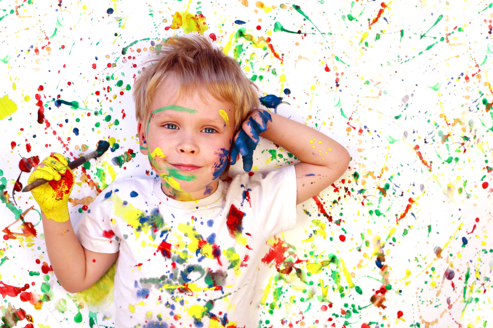 A little boy is laying on the floor covered in paint.