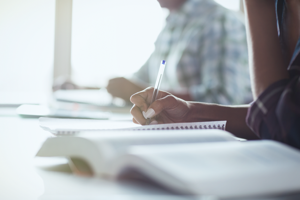 A group of people are sitting at a table writing in notebooks.