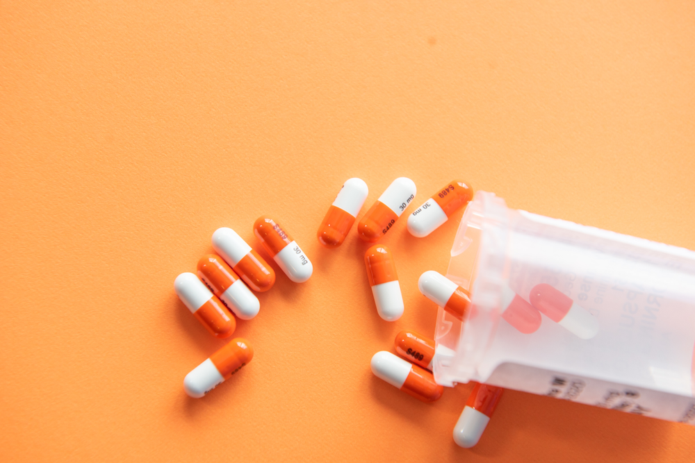 Orange and white pills are pouring out of a bottle on an orange background.