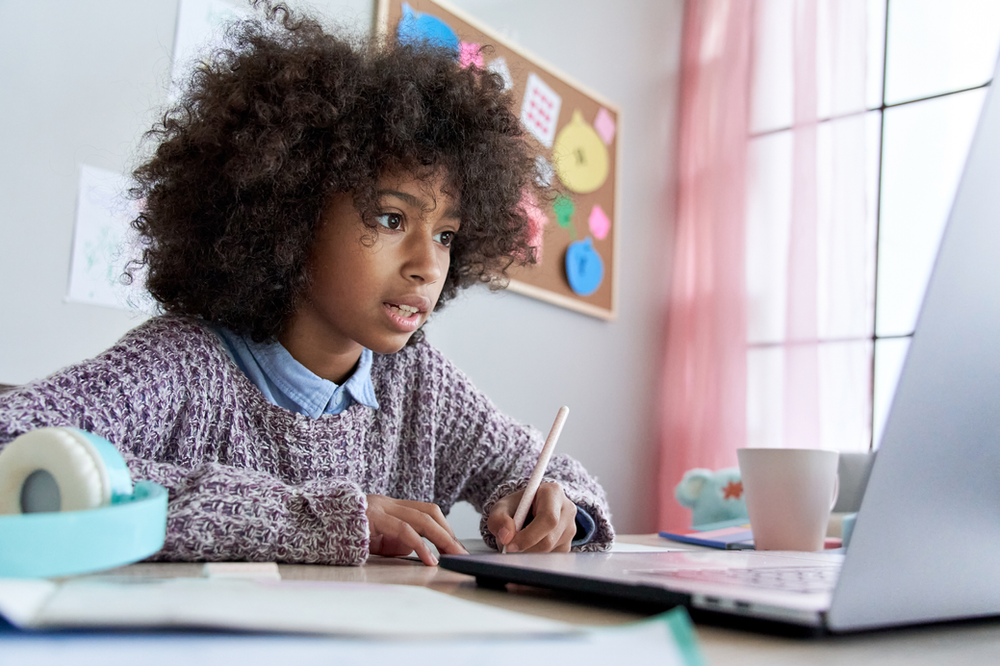 A young girl is sitting at a desk using a laptop computer.