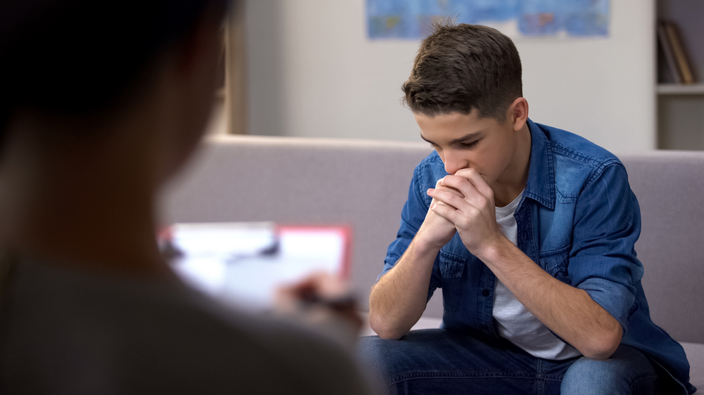 A young man is sitting on a couch talking to a therapist.