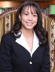 A woman in a suit is sitting in a chair and smiling.