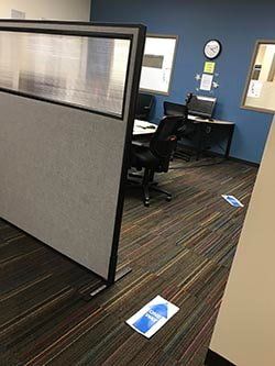 A cubicle in an office with a desk and chairs.