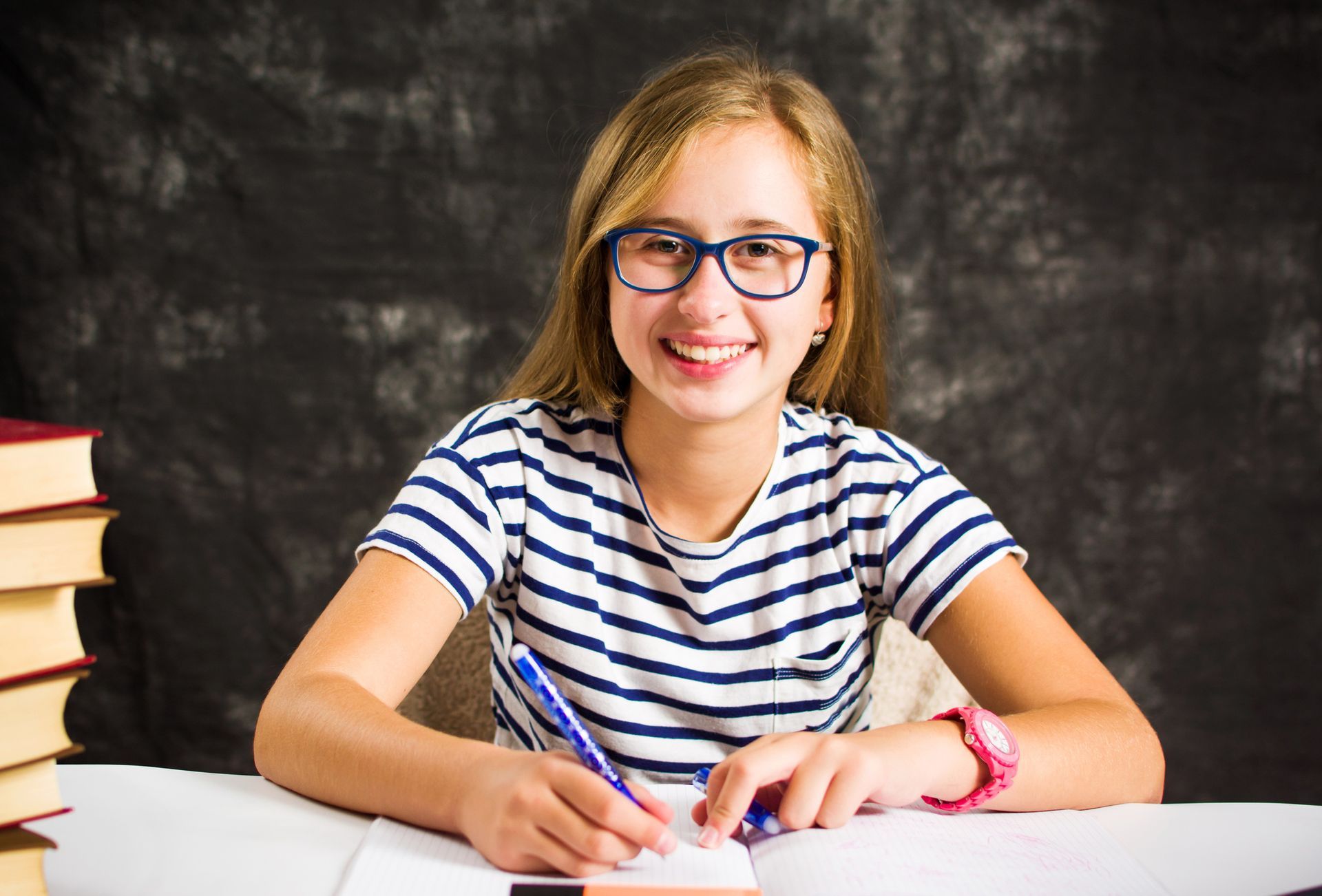 Smiling student staring at the camera while writing in notebook.