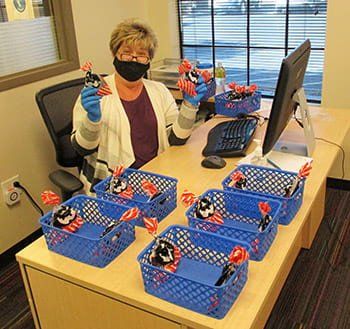 A woman wearing a mask is sitting at a desk holding a toy.