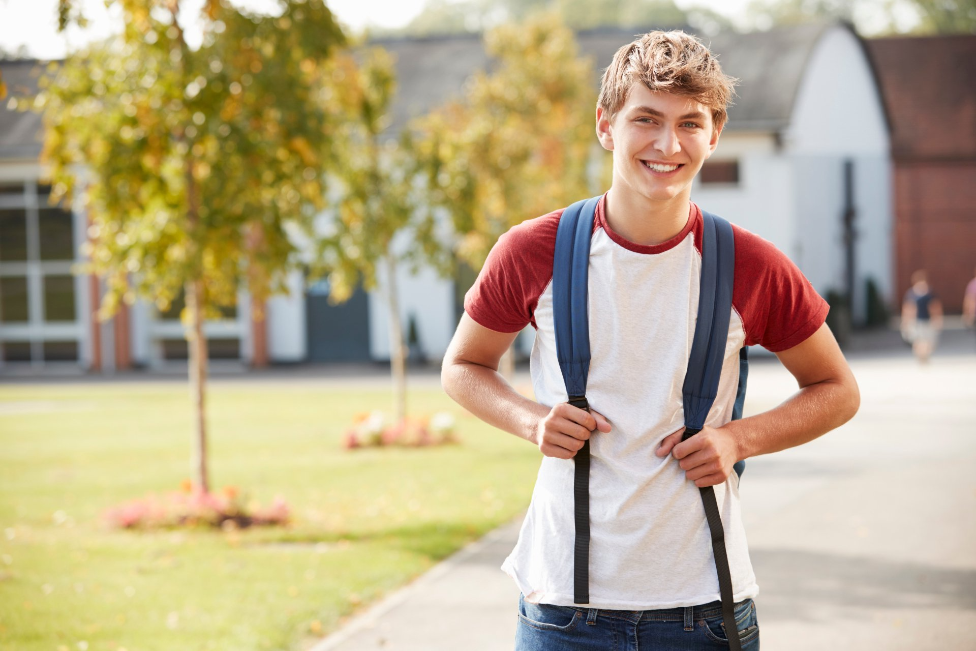 A young man with a backpack is standing on a sidewalk.