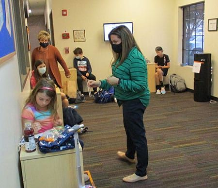 A woman wearing a mask is standing in a room with children.